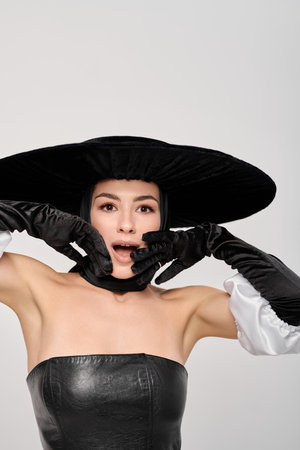 Beautiful young woman in black dress and hat with gloves on white backgroundの写真素材