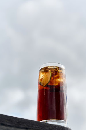 A glass of cola with ice cubes on the background of the skyの写真素材