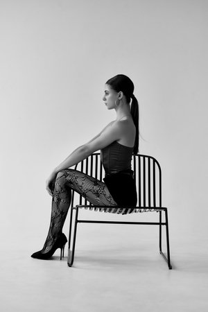 Fashionable woman in black top and black skirt posing on a chairの写真素材
