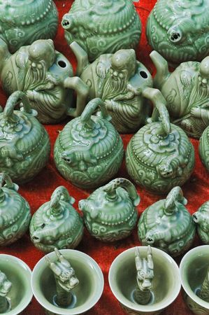 Traditional green glazed oriental ceramic teapots and cups on Chinese market bench over the red background.の写真素材