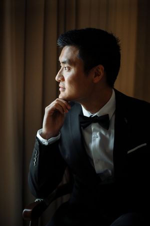 groom holds chin sitting by the window in a luxury hotelの写真素材
