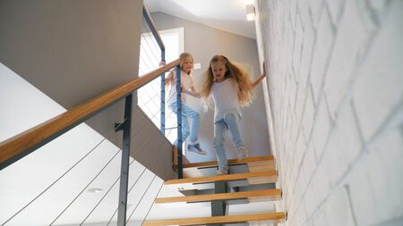 Two twin girls running down stairway while having fun at home together