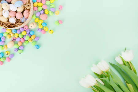 Top view of bouquet of white tulips placed near nest with colorful quail eggs on blue background on Easter Dayの写真素材