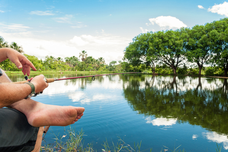 Man fishing, holding a rod on a lake with a beautiful nature around. Lake with reflection of trees on the water.の写真素材