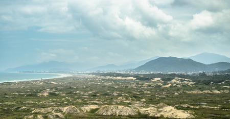 Landscape: Green vegetation growing on sand banks, sea, beach and mountains on the background. Wonderful view from a seaside town on Santa Catarina, Brazil.の写真素材