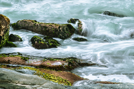 Long exposure photo of sea water running over the rocks. Rocks with green moss, beautiful scene at Morro das Pedras, Florianopolis, Brazil.の写真素材