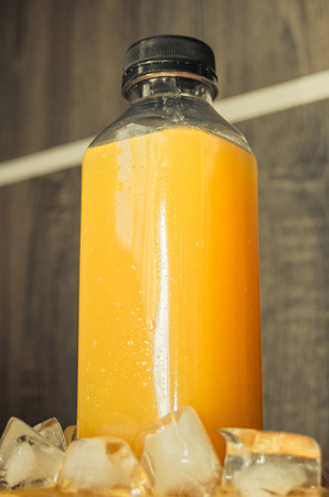 Bottle of orange juice with some ice around. Transparent plastic bottle with orange juice inside and with the black lid on a wooden background. Summer refreshing with a very cold juice.の写真素材