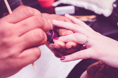 Manicurist painting the client nails with a purple nail polish. Close up on hands.の写真素材