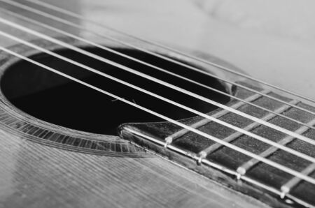Details of an old acoustic guitar, the sound hole, frets and nylon strings. Wooden acoustic guitar, worn out and dusty. Black and white, macro photo, with depth of field.の写真素材