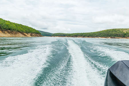 Rear view of a speedboat ride on the lake making waves and the landscape of the Lake of Furnas at...
