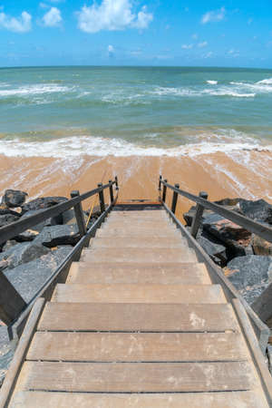 Beachfront landscape of a wooden stair leading down to the sea, beautiful blue sky day. Boa Viagem beach in Recife, PE, Brazil.の写真素材