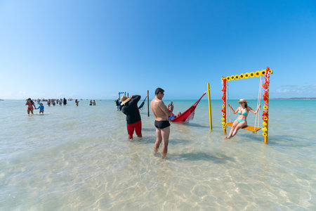 Maragogi, AL, Brazil - October 17, 2021: tourists taking photos on the decorated swing and hammocks in the middle of the sea at Moses Path, Barra Grande beach.のeditorial素材