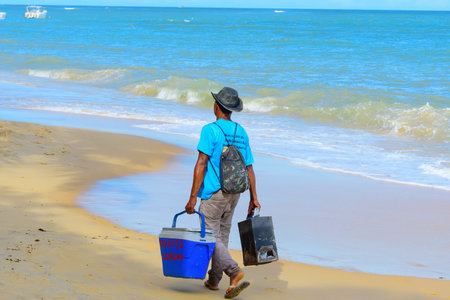 Porto Seguro, BA, Brazil - January 07, 2023: street vendor of coalho cheese walking on the sand of Espelho Beach.のeditorial素材