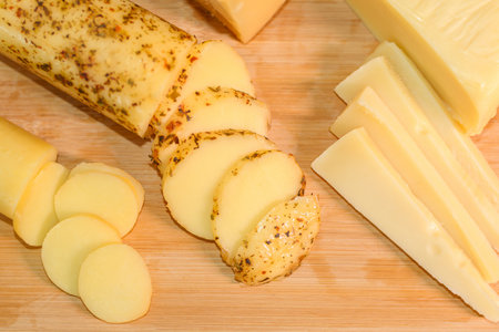 Wooden cutting board with thinly sliced provolone cheese, seasoned provolone cheese, and gruyere cheese slices.の写真素材