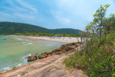 Guaiuba Beach, Guaruja SP, Brazil. Sunny day over the small bay with tranquil sea. Image of leisure and tourism on the Sao Paulo coast. Hills covered in Mata Atlantica vegetation frame the view.の写真素材