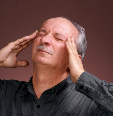 Portrait of a senior man suffering from a bad headache on a brown background の写真素材