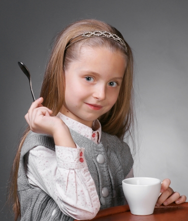 Little girl with cup of tea holding a spoon in hand on a gray ackgroundの写真素材