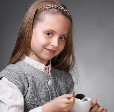 Little girl with cup of tea holding a spoon in hand on a gray ackgroundの写真素材