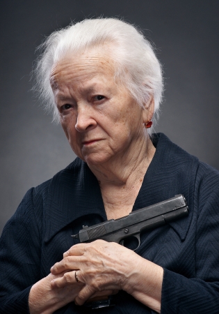 Close-up portrait of old woman with pistol on a gray background の写真素材