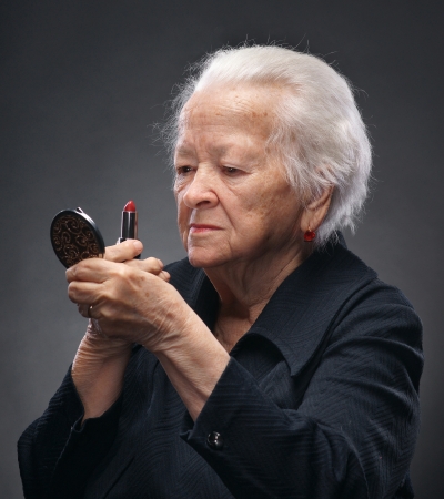 Closeup portrait of old woman with lipstick and mirror on a gray backgroundの写真素材
