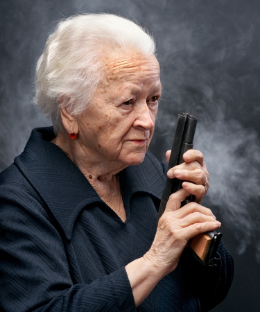 Portrait of old woman with pistol in smoke on a dark backgroundの写真素材