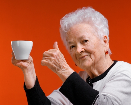Old woman in glasses enjoying coffee or tea cup over orange backgroundの写真素材