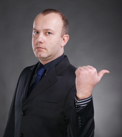 Portrait of a serious young businessman pointing at something on a gray backgroundの写真素材