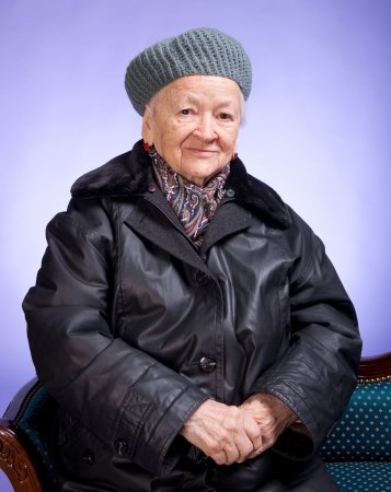 Smiling old woman sitting on a chair on a lilac backgroundの写真素材