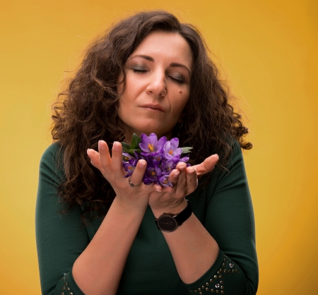 Curly woman smelling crocus flowers with close eyes on a yellow backgroundの写真素材