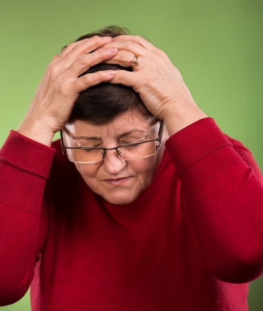 Mature woman suffering from a headache on a green backgroundの写真素材