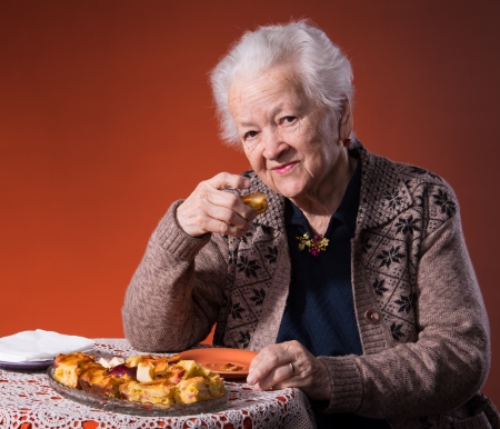 Senior woman tasting apple pie on an orange backgroundの写真素材