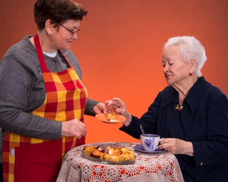 Mother and daughter having tea with apple pie on an orange  backgroundの写真素材