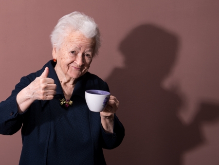 Old woman enjoying coffee or tea cup over brown backgroundの写真素材
