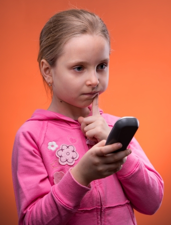 Upset girl holding phone on an orange backgroundの写真素材