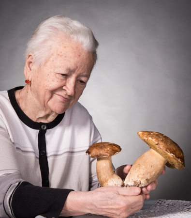 Old woman looking at mushrooms on a gray backgroundの写真素材