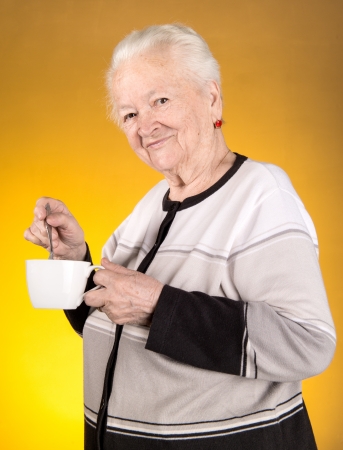 Old woman enjoying coffee or tea cup over yellow backgroundの写真素材