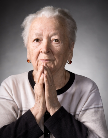 Old woman praying on a gray backgroundの写真素材