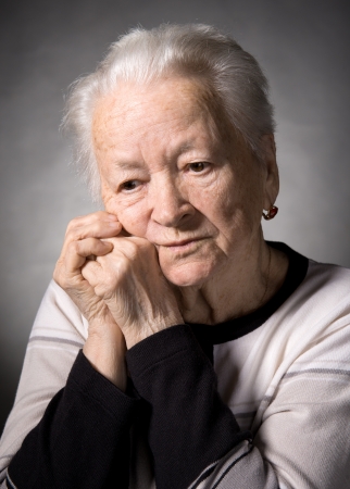 Old  thoughtful woman on a gray backgroundの写真素材