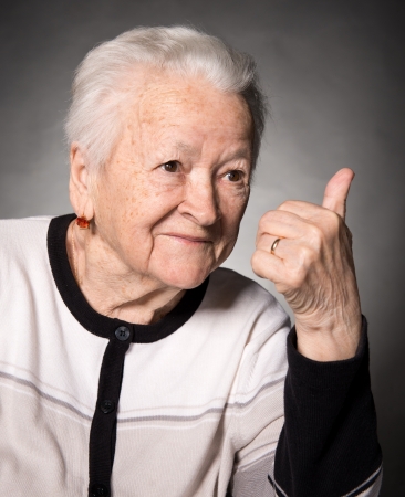 Old woman showing ok sign on a gray backgroundの写真素材