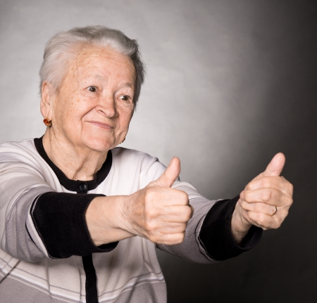 Old woman showing ok sign on a gray backgroundの写真素材