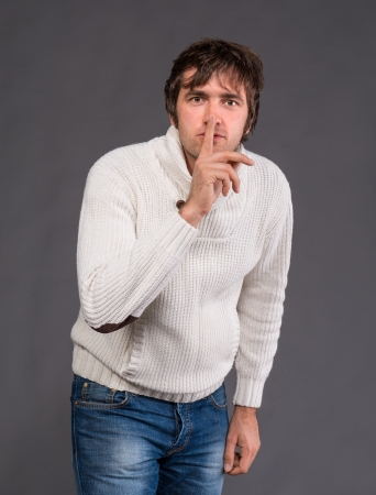 Handsome man with finger on lips asking for silence on a gray backgroundの写真素材