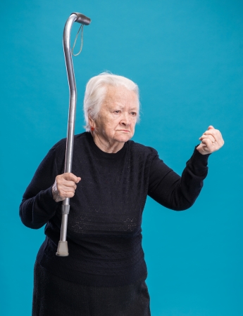 Old angry woman threatening with a cane on a blue backgroundの写真素材