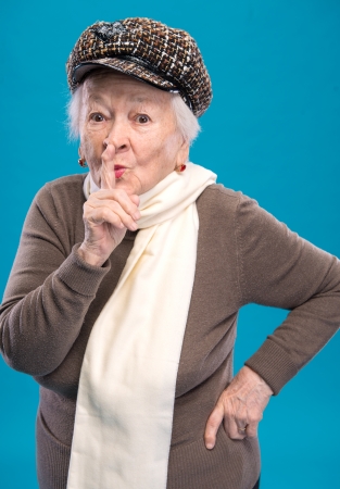 Old woman with finger on lips asking for silence on a blue backgroundの写真素材