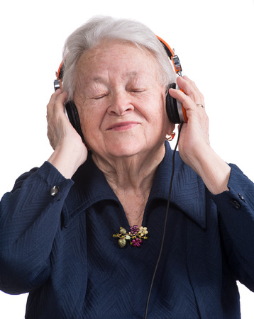Old woman listening to music in headphones on a white の写真素材