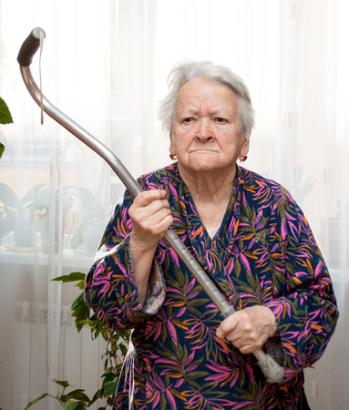 Old angry woman threatening with a cane at homeの写真素材