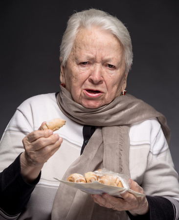Old woman choking with cookie on a gray の写真素材