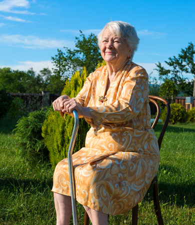 Old woman sitting on a chair with a cane in the gardenの写真素材