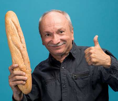 Happy senior man holding fresh baguette on a blue backgroundの写真素材