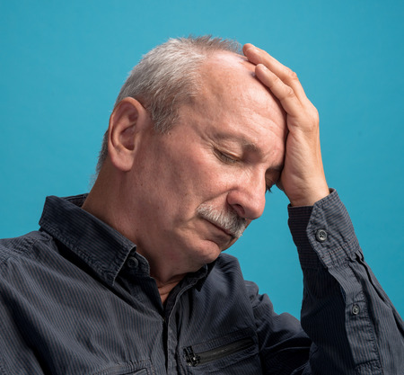 Headache  Portrait of senior man on a blue backgroundの写真素材