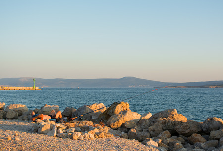 Fisherman relaxing near fishing rod at the beach in the evening lightの写真素材